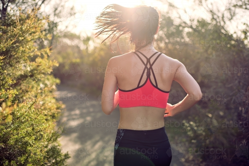 Fit Asian woman running for morning exercise, with lens flare - Australian Stock Image