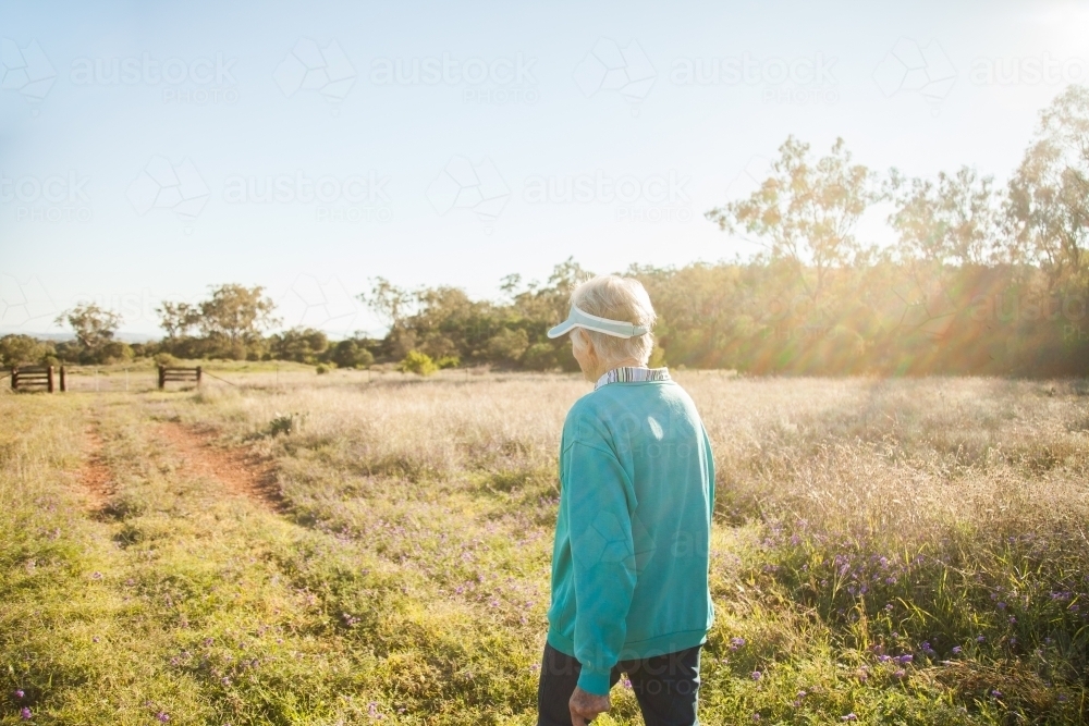 Fit elderly woman walking along track in paddock - Australian Stock Image