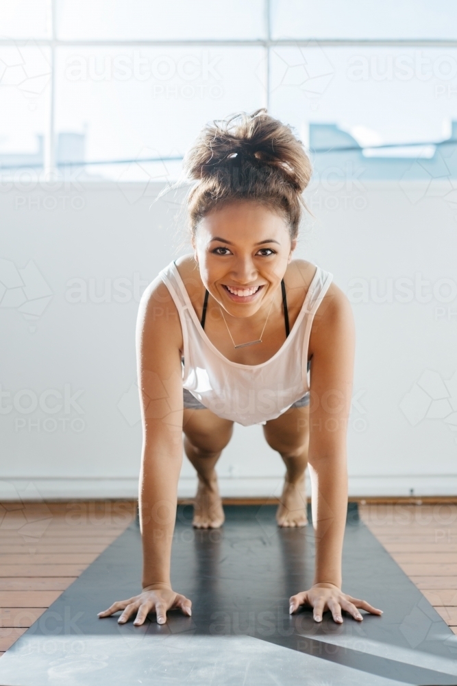 Fit girl performing a plank in a gym smiling at camera - Australian Stock Image