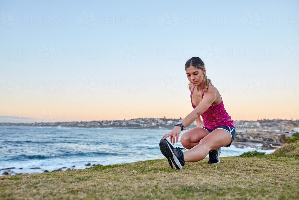 Fitness woman warming up and stretching at coastal headland - Australian Stock Image