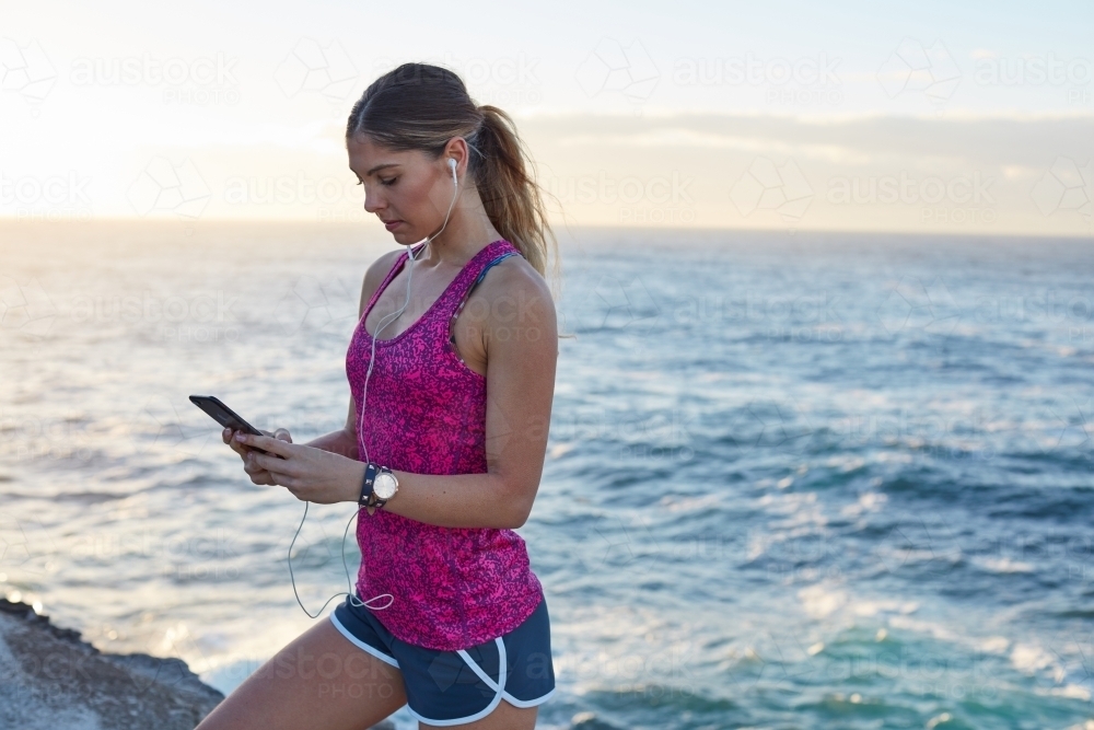 Fitness woman with phone at coastal headland on sunrise - Australian Stock Image