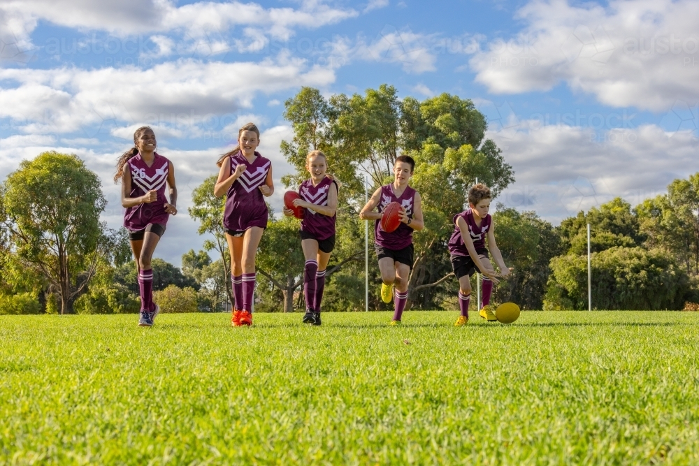 five children in football uniforms running on green grass - Australian Stock Image