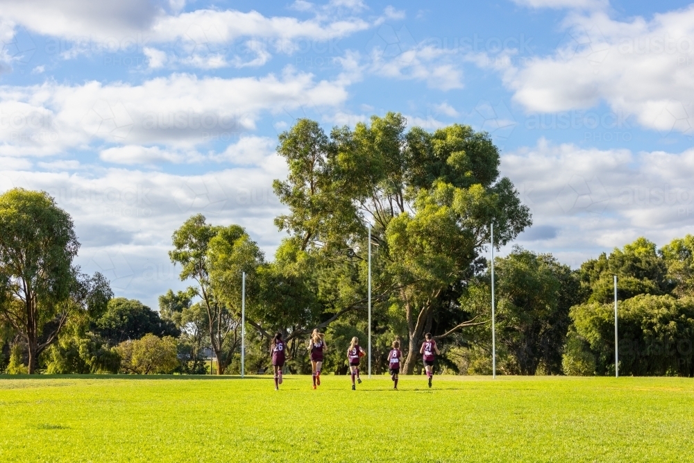 Image of five children running away towards goal posts on football oval ...