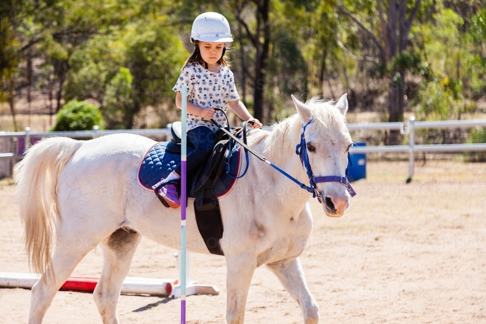 Five year old horse rider doing pole bending on white pony - Australian Stock Image