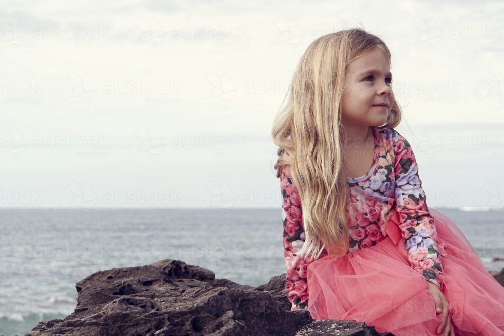 Five year old sitting on rock at beach looking away - Australian Stock Image