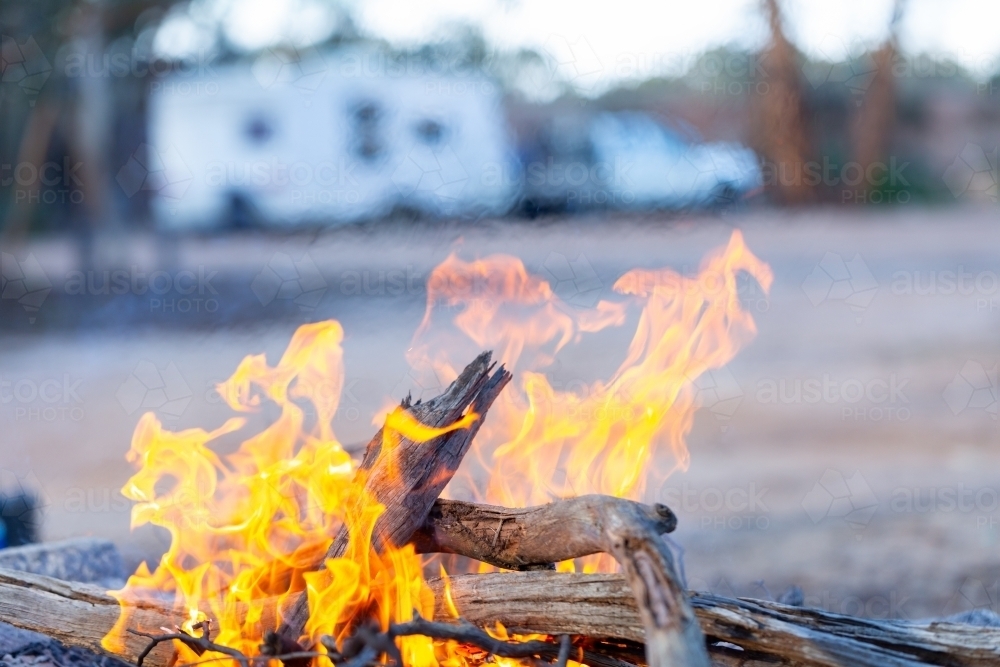 flames of campfire in foreground with caravan in background - Australian Stock Image