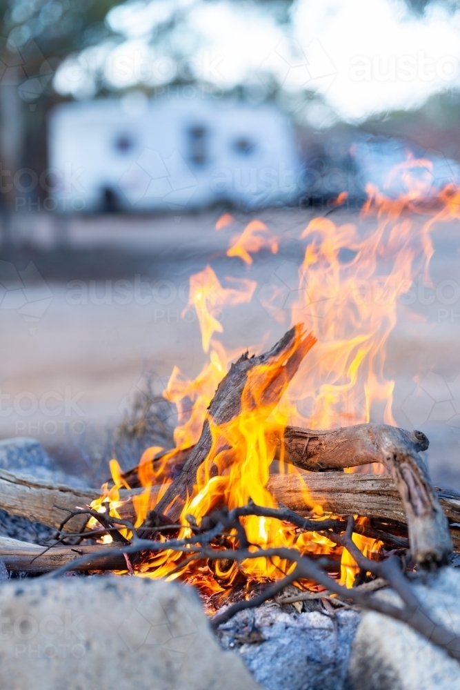 flames of campfire in foreground with caravan in background - Australian Stock Image