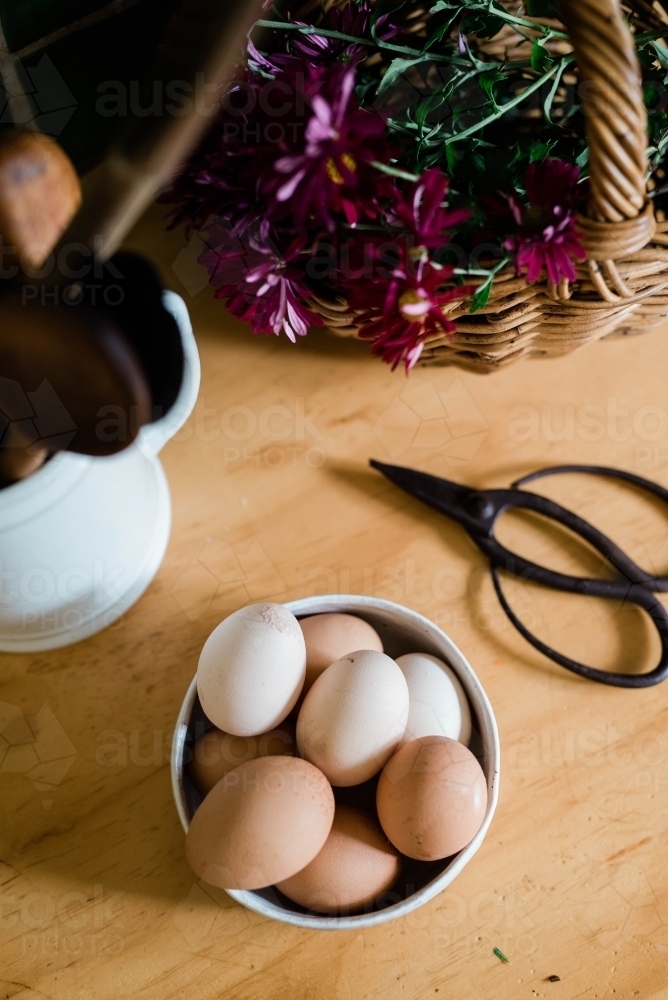Flat lay of bowl of eggs, floral scissors, basket of flowers and cup of utensils - Australian Stock Image