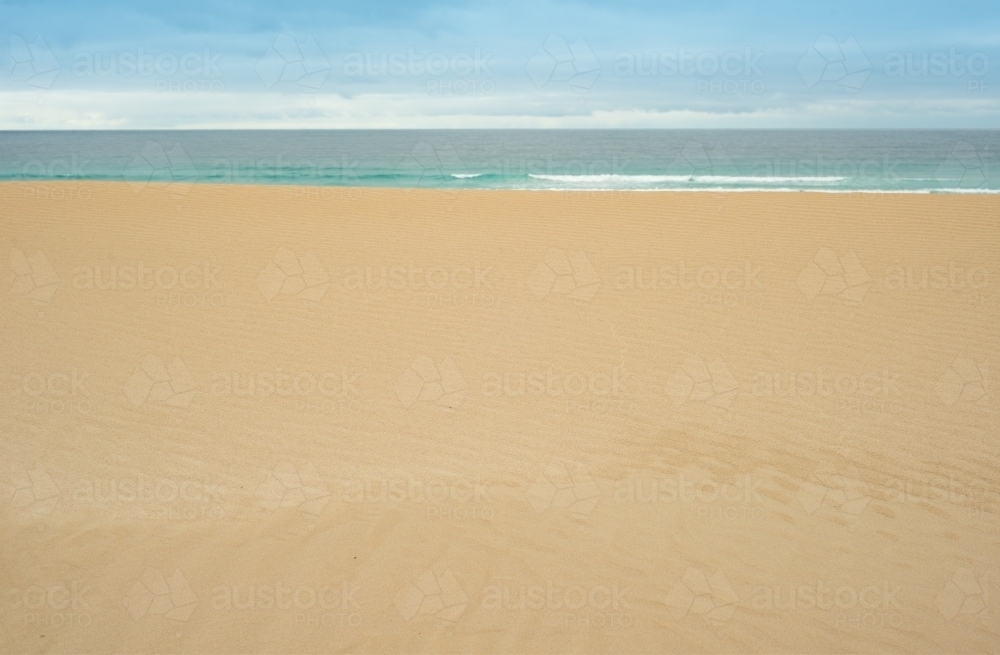 Flat, untouched sand leading to calm ocean in the background - Australian Stock Image