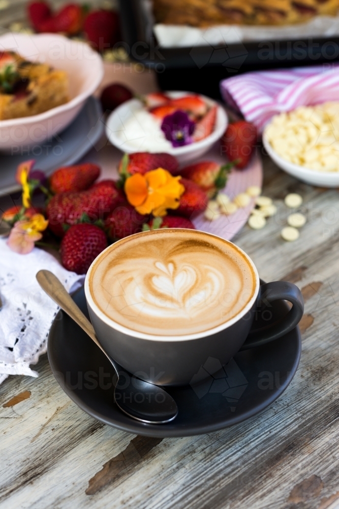 flat white coffee with love heart latte art, on a cafe table with dessert and strawberries - Australian Stock Image