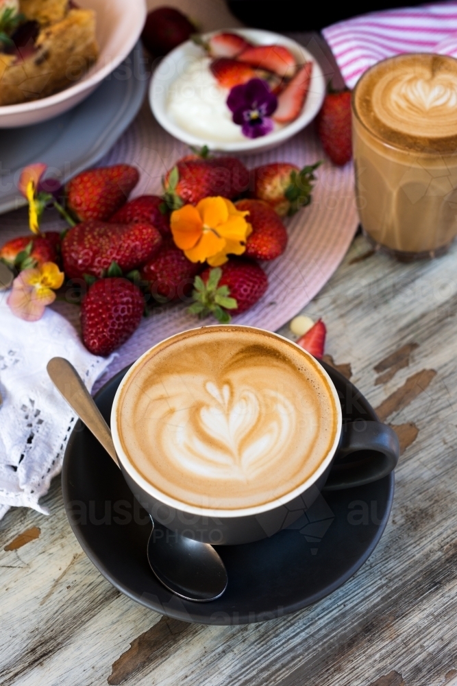 flat white coffee with loveheart latte art, on a cafe table with dessert and strawberries - Australian Stock Image