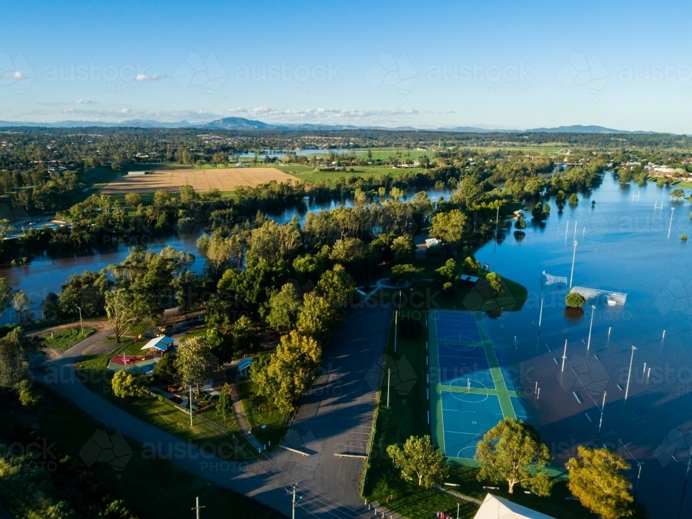 Flooded netball courts and park beside overflowing river with water levels still rising - Australian Stock Image