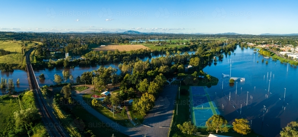 Flooded netball courts and park beside overflowing river with water levels still rising - Australian Stock Image