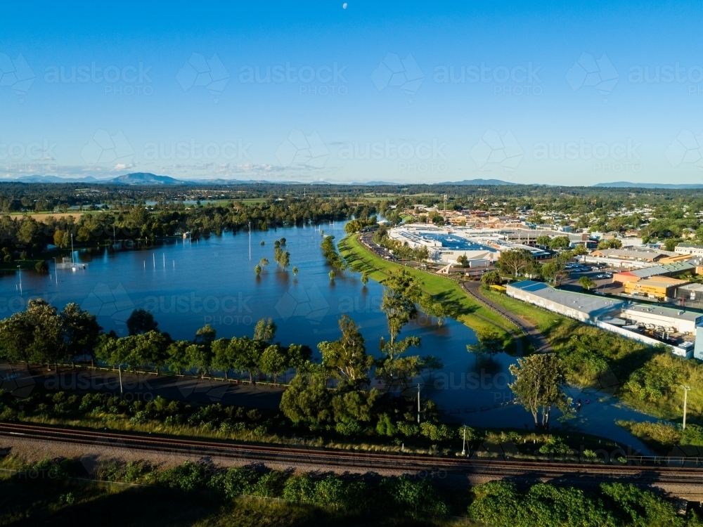 Flooded playing fields and park with floodwater rising up levee bank towards town and shops - Australian Stock Image