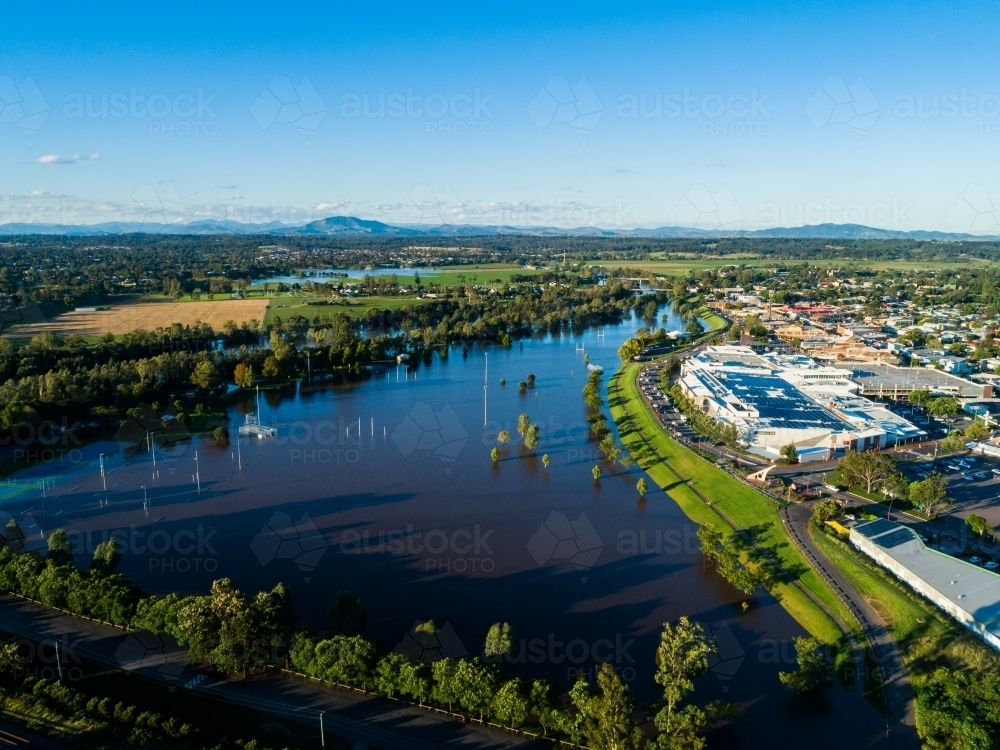 Flooded playing fields and park with floodwater rising up levee bank towards town and shops - Australian Stock Image