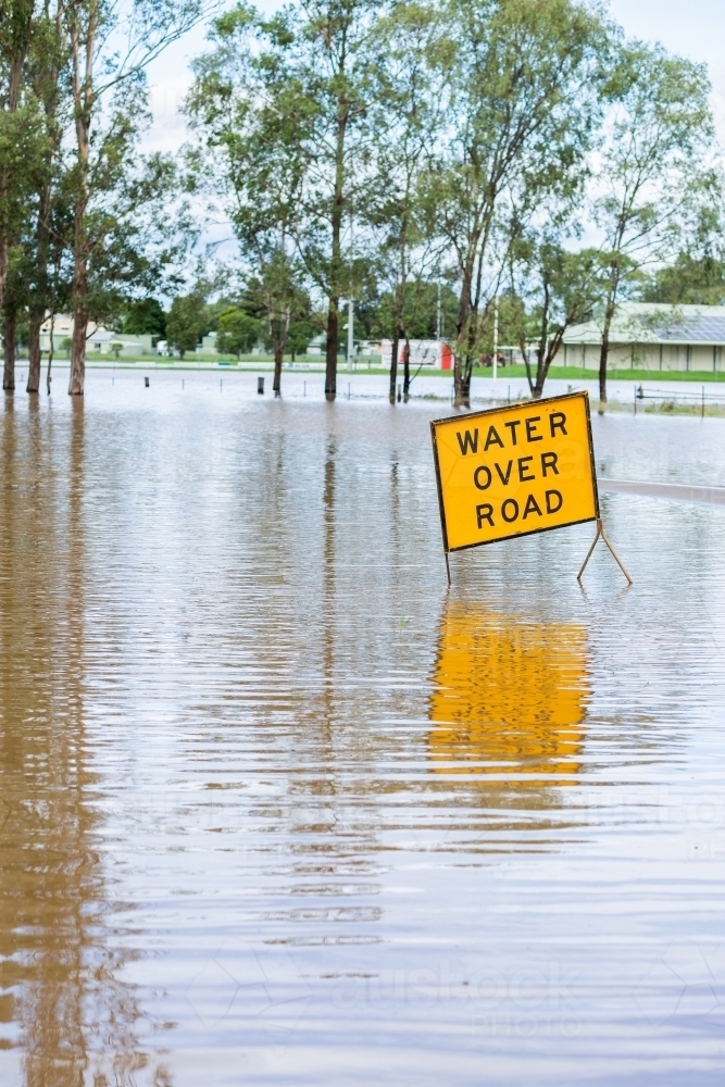 Floodwater rising over water over road sign on highway - Australian Stock Image