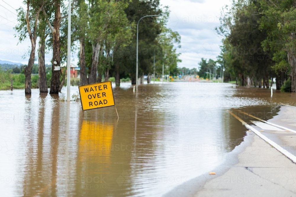 Floodwater rising over water over road sign on highway - Australian Stock Image