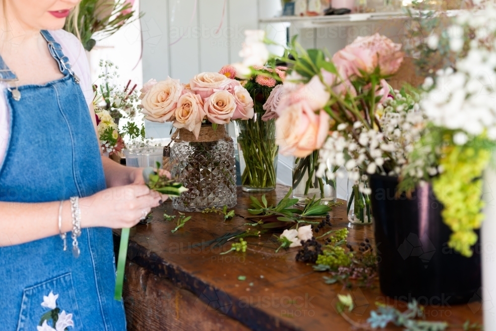 Florist preparing wedding buttonholes at a work bench full of flowers - Australian Stock Image