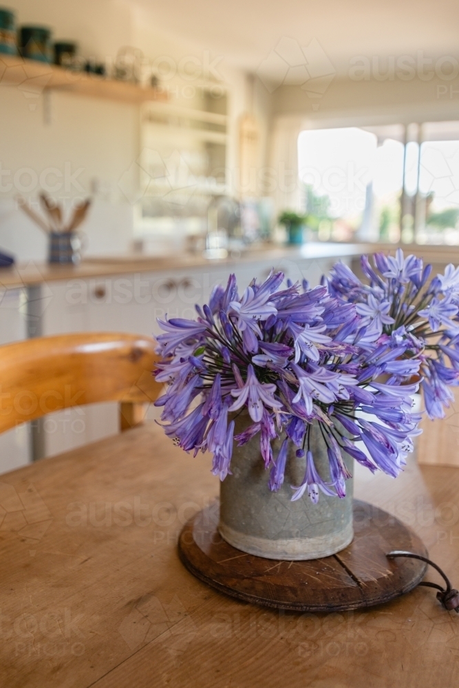 flowers in a vase on a timber dining table, kitchen in background - Australian Stock Image