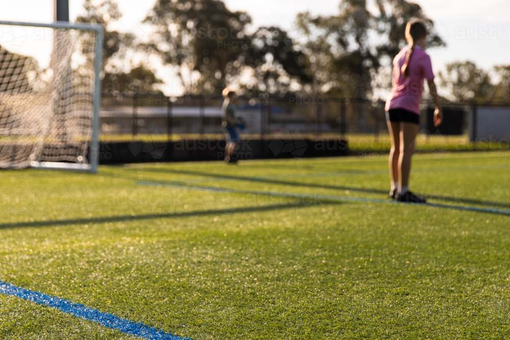 focus on foreground kids playing soccer on artificial turf field - Australian Stock Image
