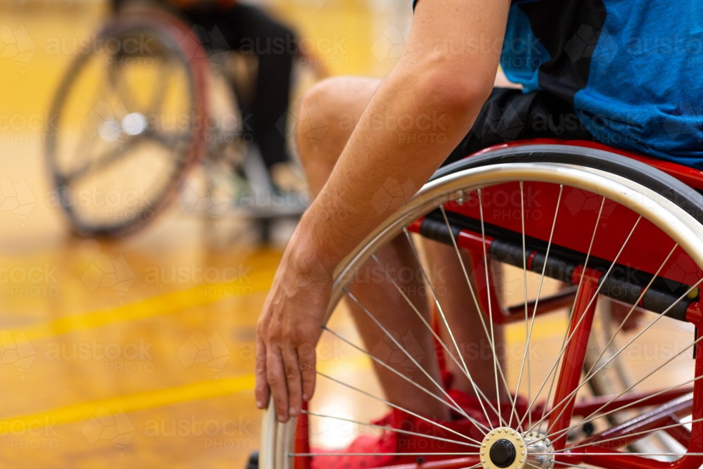 focus on one arm and wheelchair wheel with spokes and another blurry wheelchair in background - Australian Stock Image