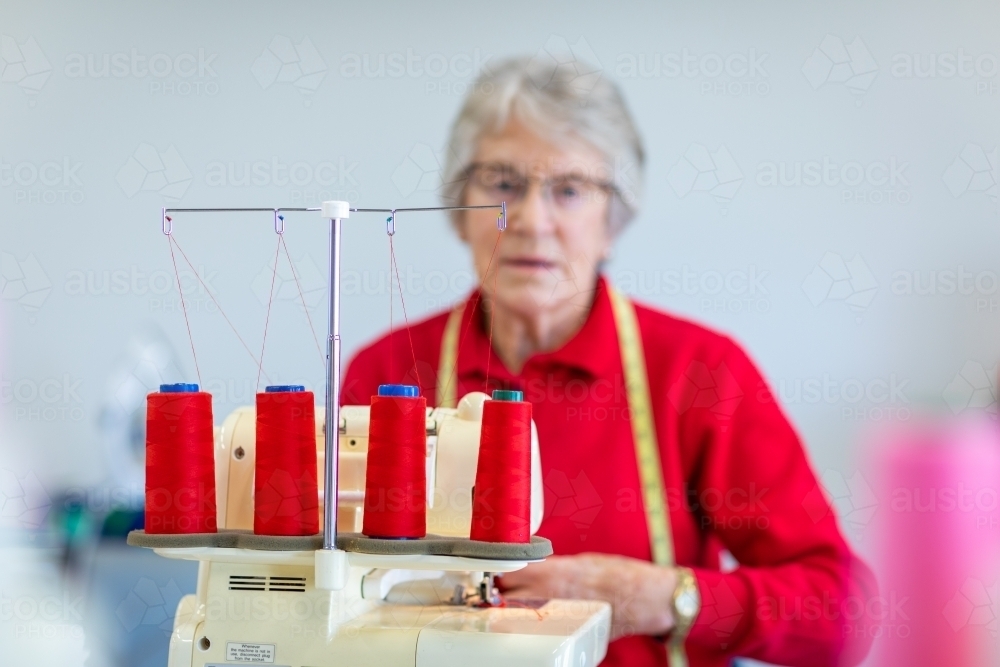 focus on red thread with elderly lady blurred behind sewing machine - Australian Stock Image