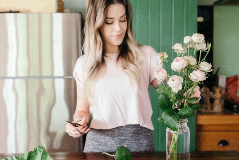 Focus on the pink roses with blurred woman in background cutting stems and arranging - Australian Stock Image