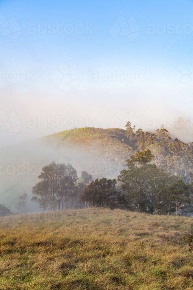Fog blowing away over mountain top with the coming of the sun - Australian Stock Image