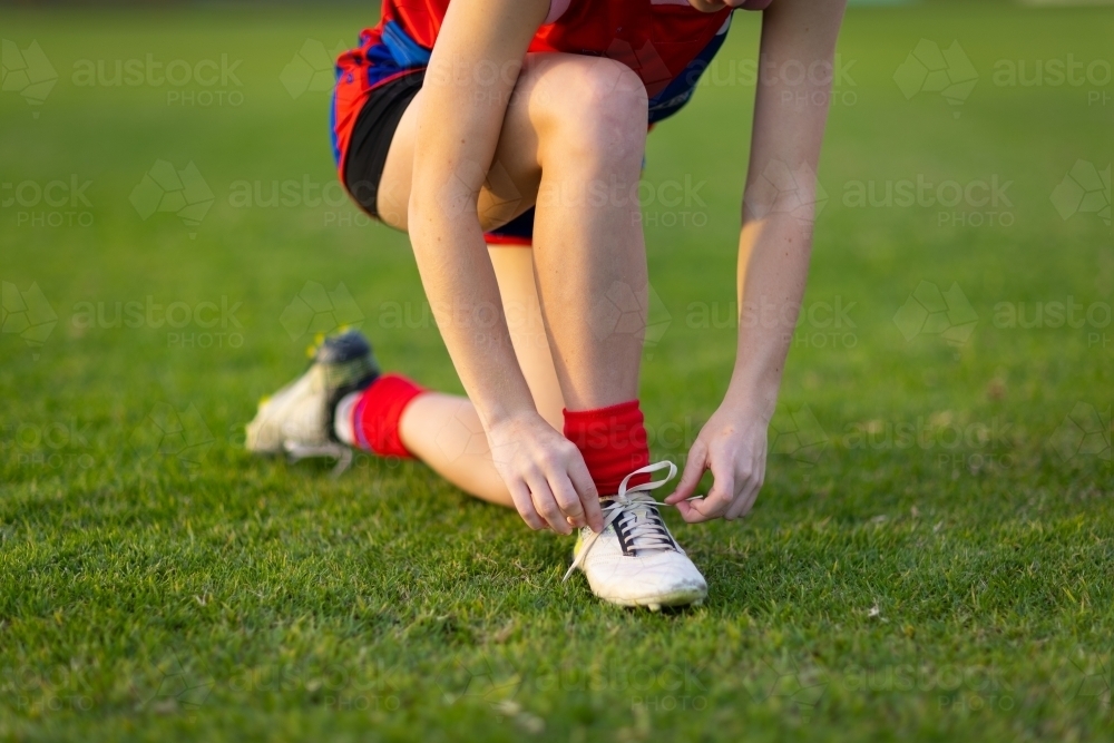 footballer wearing red socks kneeling down to tie bootlace - Australian Stock Image