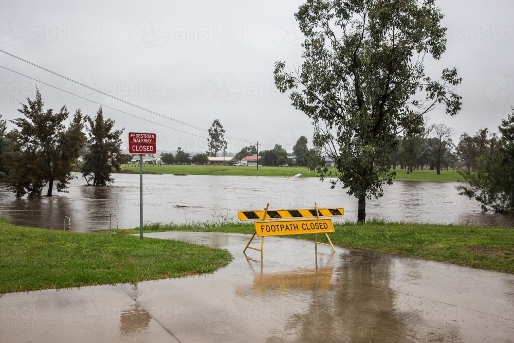 Footpath closed sign in front of path under water from extreme flooding - Australian Stock Image