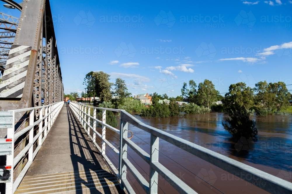 Footpath on side of bridge overlooking brown floodwaters or raging river - Australian Stock Image