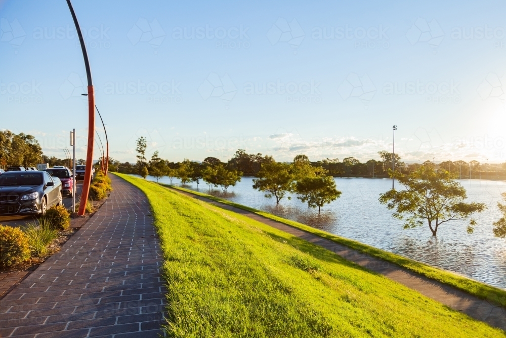 footpath with hill down levee bank in singleton with floodwaters covering playing field - Australian Stock Image