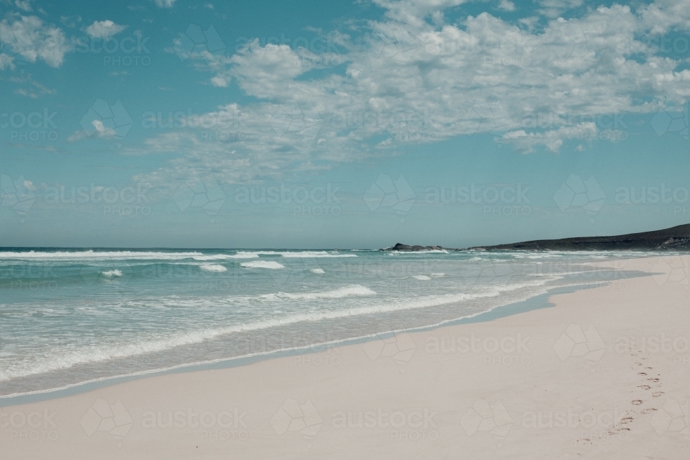 Footprints in white sand on the shore of clear water at the beach - Australian Stock Image