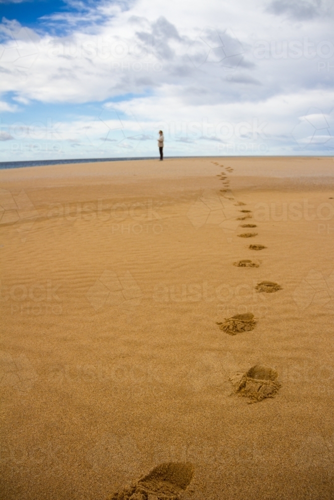 Footprints on a beach leading to a person in the distance - Australian Stock Image