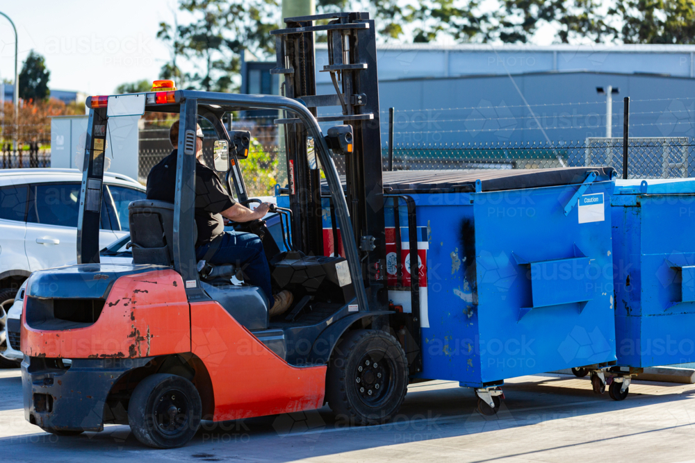 Image of Forklift operator using machinery to move industrial bins ...