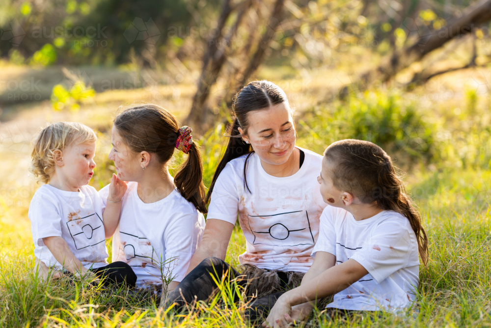 Four Aboriginal Australian siblings together in long green grass by riverside in bushland - Australian Stock Image