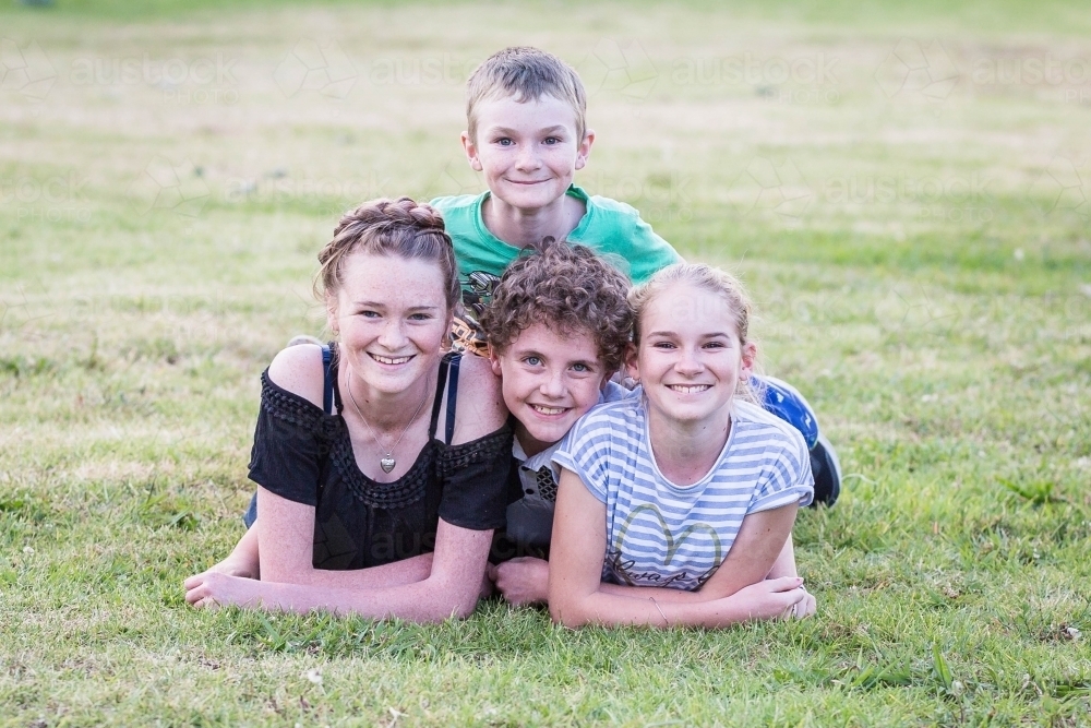 Four children family lying on grass together smiling - Australian Stock Image