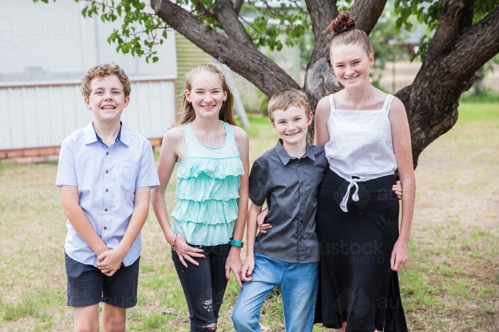 Four children standing together in yard at home smiling happy - Australian Stock Image