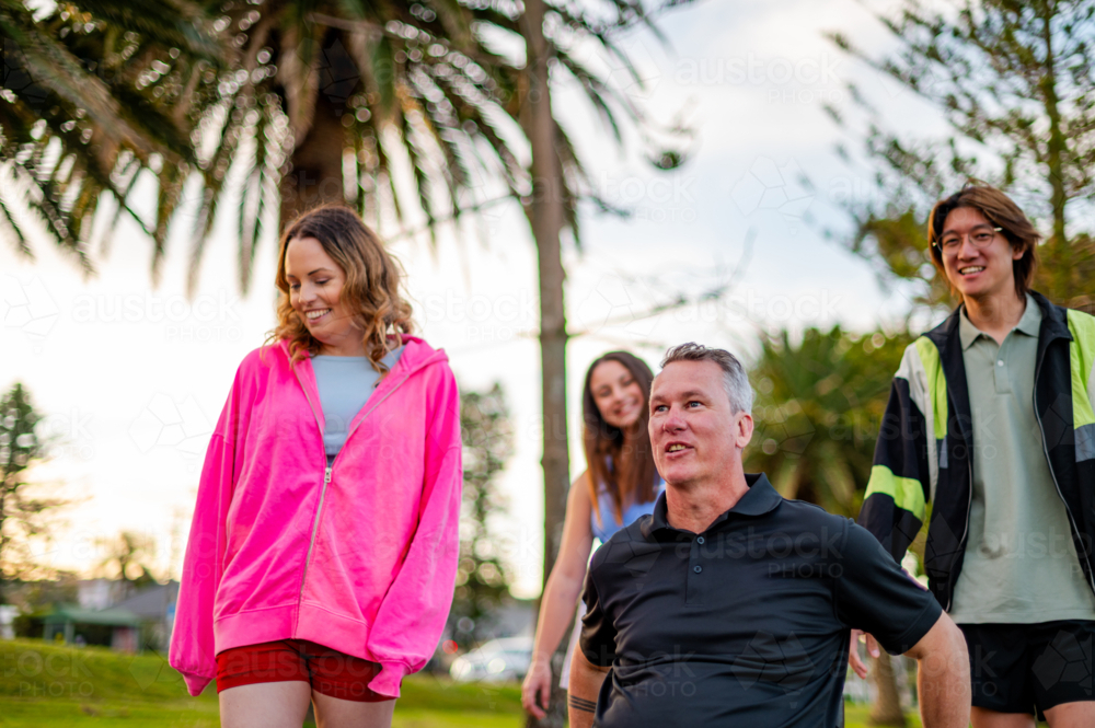 Four friends walk together in a park, laughing and enjoying the warm afternoon sun - Australian Stock Image