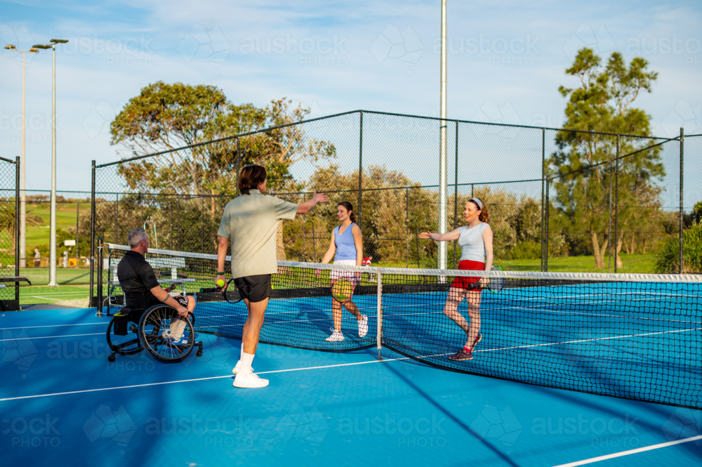 Four individuals participate in an inclusive tennis match on bright blue courts outdoors - Australian Stock Image