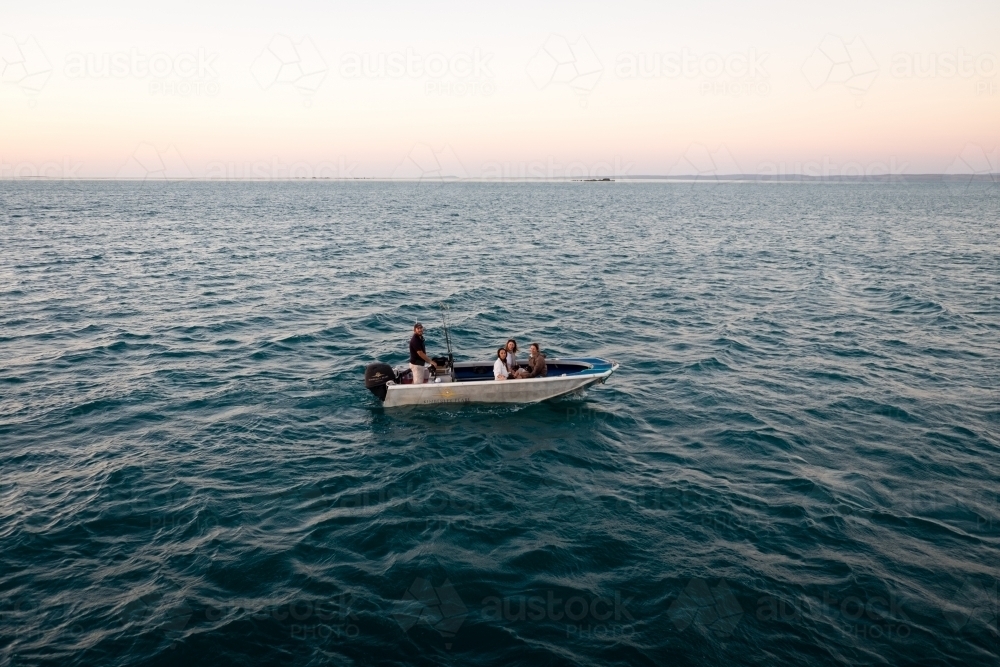 Four people sitting in a dinghy in remote ocean at sunset - Australian Stock Image