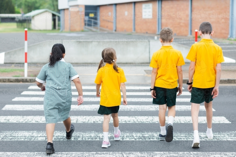 Four school kids walking across a pedestrian crossing - Australian Stock Image