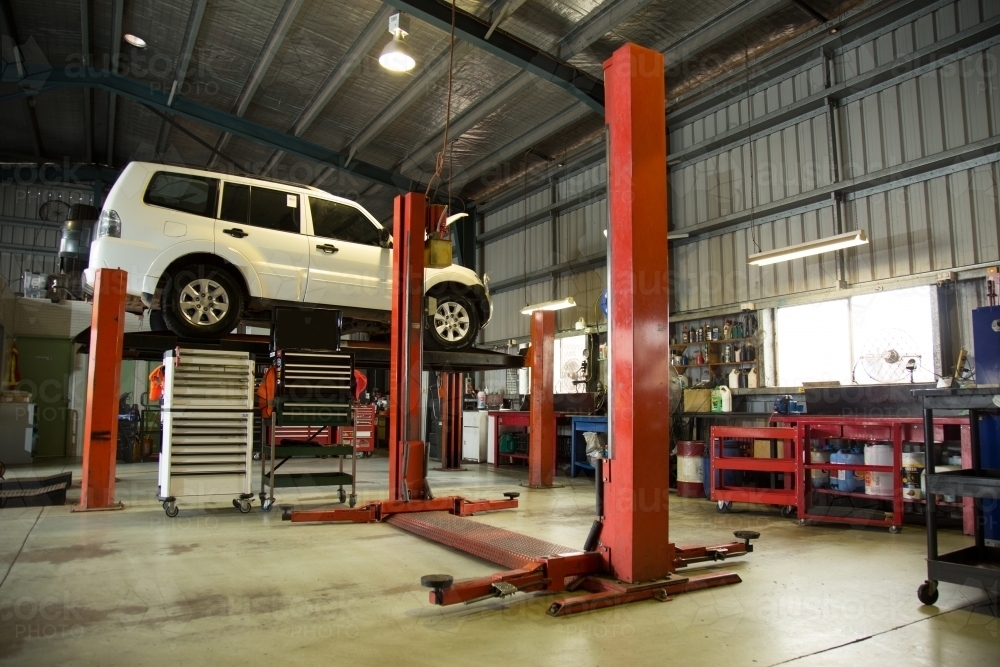 Four wheel drive lifted in hoist for repairs in a mechanic workshop - Australian Stock Image
