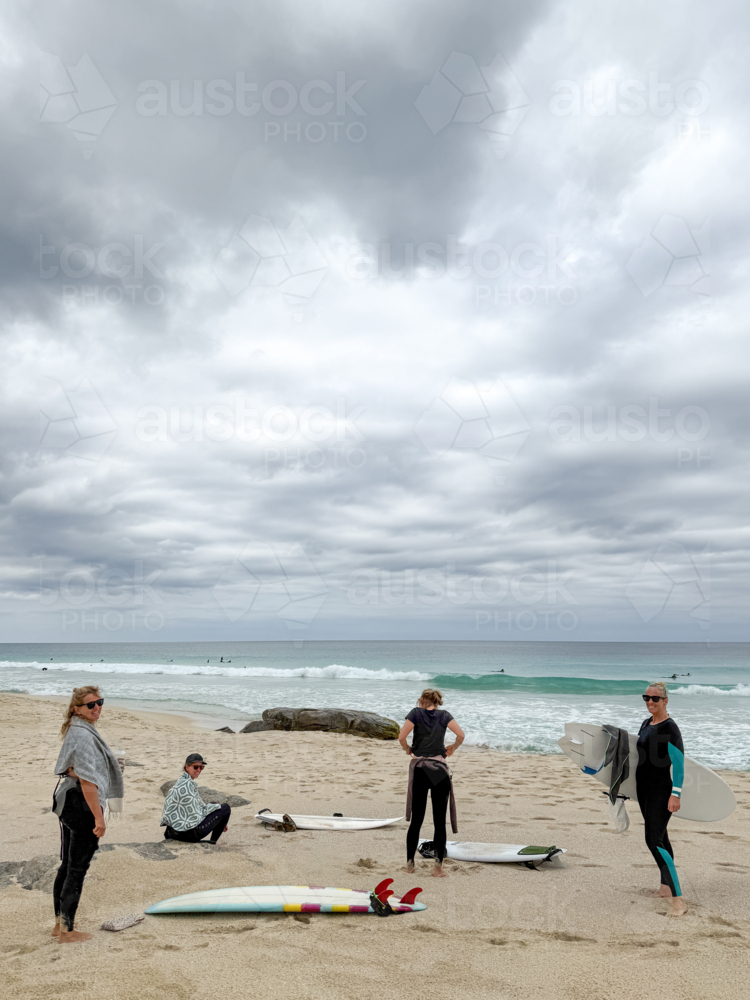 Four women on beach getting ready to surf waves on overcast day - Australian Stock Image