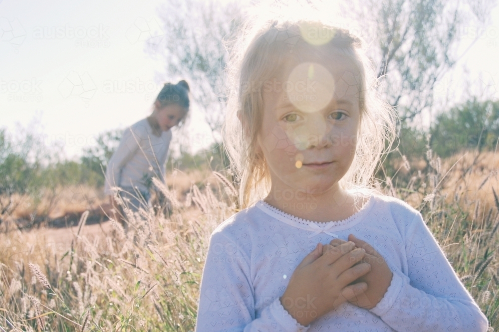 Four year old girl standing in a paddock with sun flare - Australian Stock Image