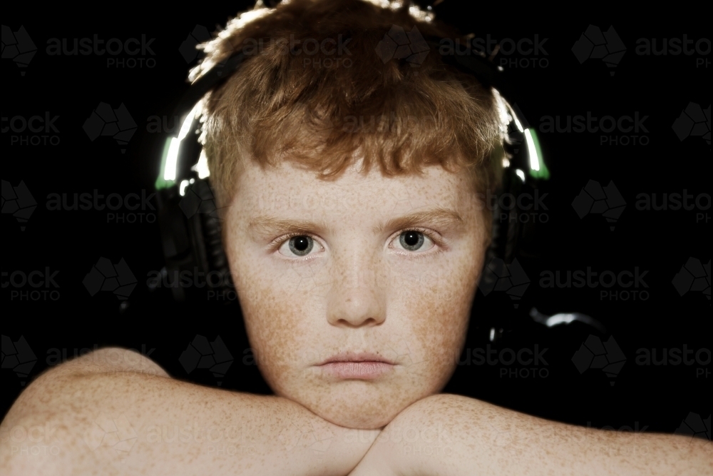 freckled teenage boy looking at cameras with headphones on - Australian Stock Image