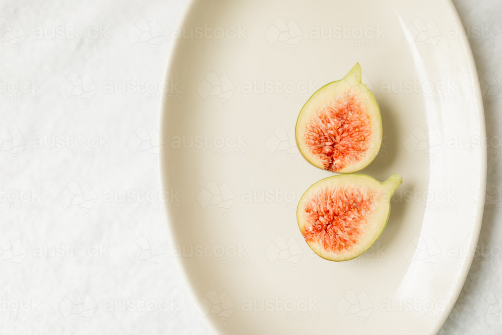 Fresh fig fruit cut in half on plain white plate - Australian Stock Image