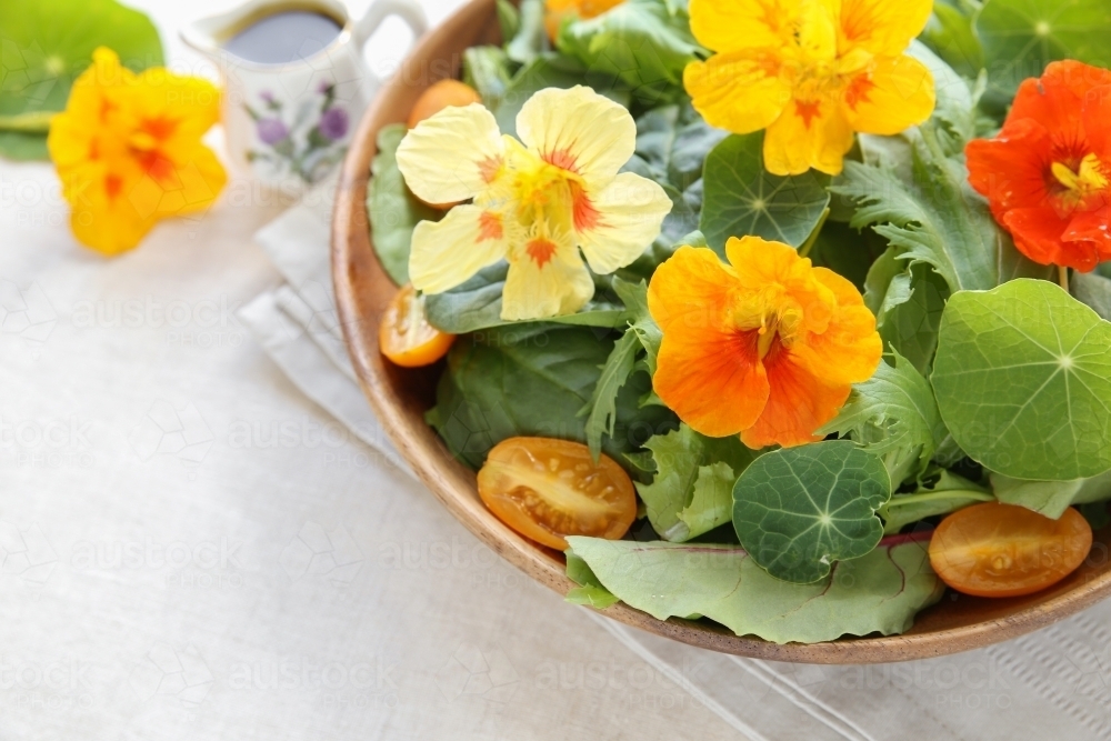 Fresh green salad with edible flowers nasturtium in wooden serving dish - Australian Stock Image