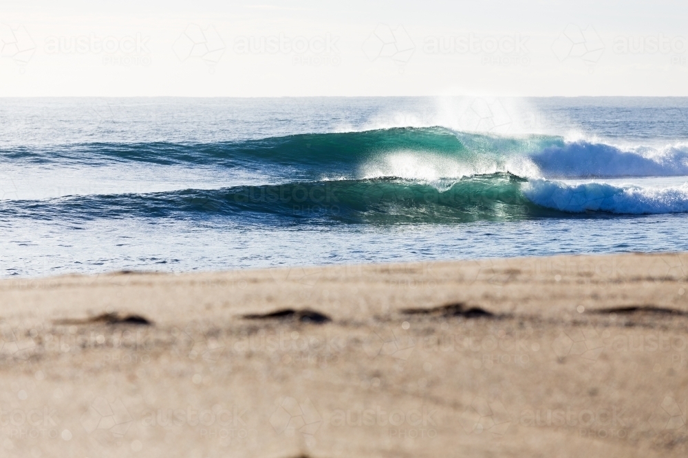 Fresh ocean waves breaking in bright morning light towards a beautiful sandy beach with footprints - Australian Stock Image