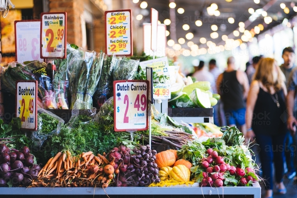 Fresh produce market with prices and vegetables in focus and people in background - Australian Stock Image